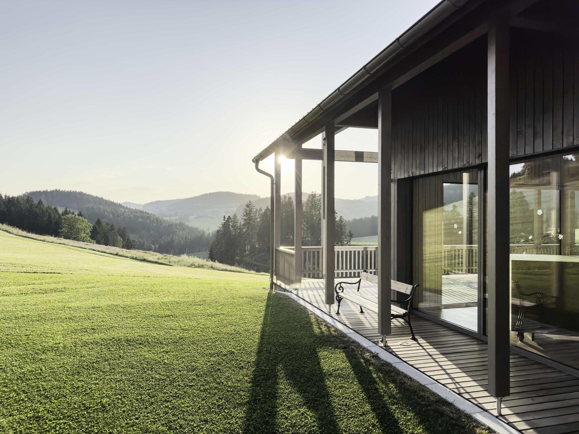 Bauen mit Holz_Holzhaus mit Terrasse in saftig grüner hügeliger Landschaft